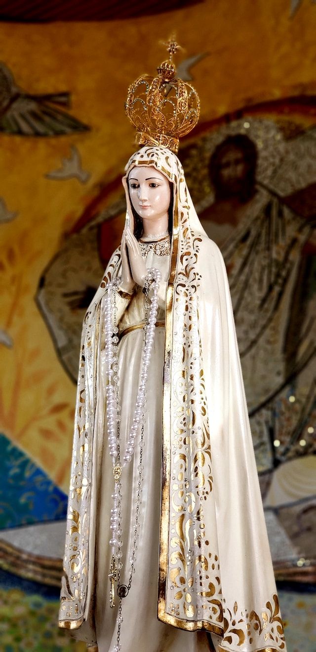La virgen de Fátima tiene una gran corona dorada, vestido y manto blanco